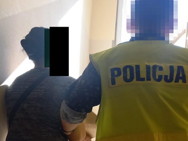 Policjant eskortujący kobietę, na kamizelce widoczny napis POLICJA