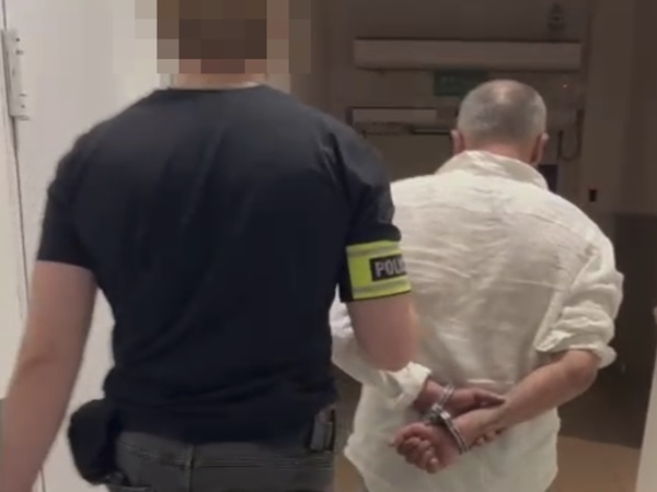 Policjant eskortujący skutego mężczyznę na korytarzu szpitalnym.