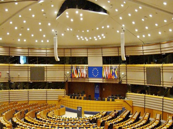 Sala posiedzeń Parlamentu Europejskiego w Brukseli, na której widać puste krzesła i flagi państw członkowskich UE.