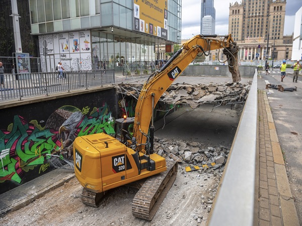 Żółta koparka burzy część drogi.