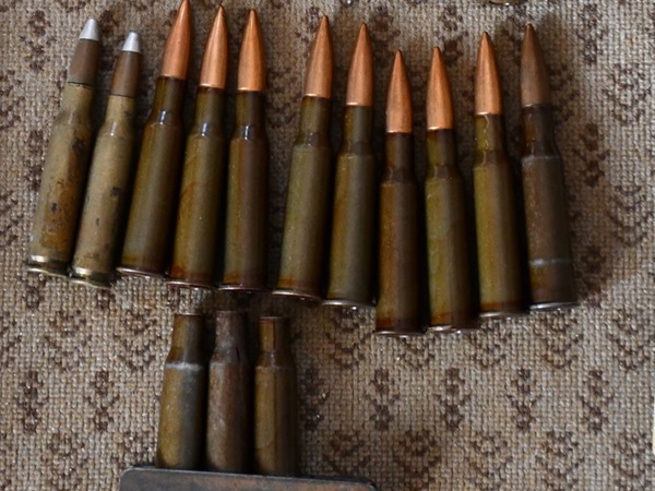 Różne naboje karabinowe i amunicja ułożone na teksturowanej powierzchni.