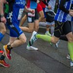 Biegacze rywalizują w biegu ulicznym, prezentując obuwie sportowe i skarpetki uciskowe.