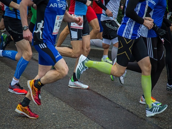 Biegacze rywalizują w biegu ulicznym, prezentując obuwie sportowe i skarpetki uciskowe.