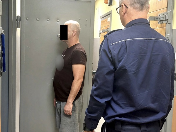 Więzień stojący pod ścianą podczas kontroli bezpieczeństwa