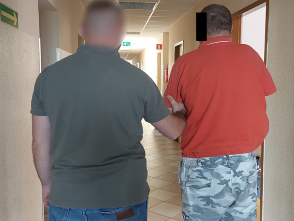 Widok z tyłu dwóch mężczyzn idących korytarzem, ręka jednego z nich spoczywa na ramieniu drugiego.