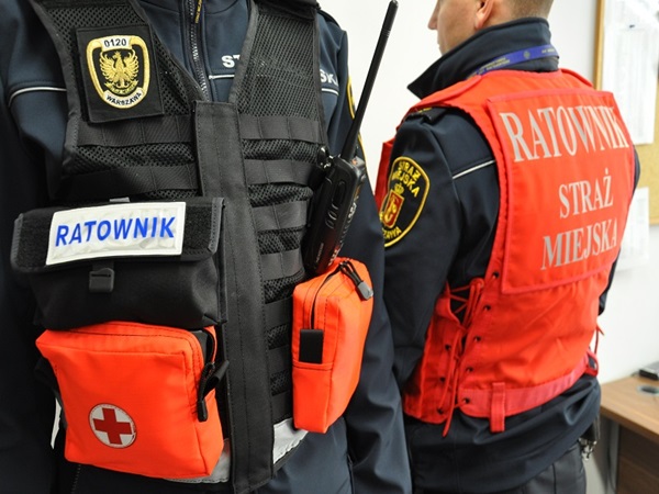 Dwóch strażaków z polskiej straży pożarnej w kamizelkach odblaskowych z napisem „Ratownik Straż Miejska”.