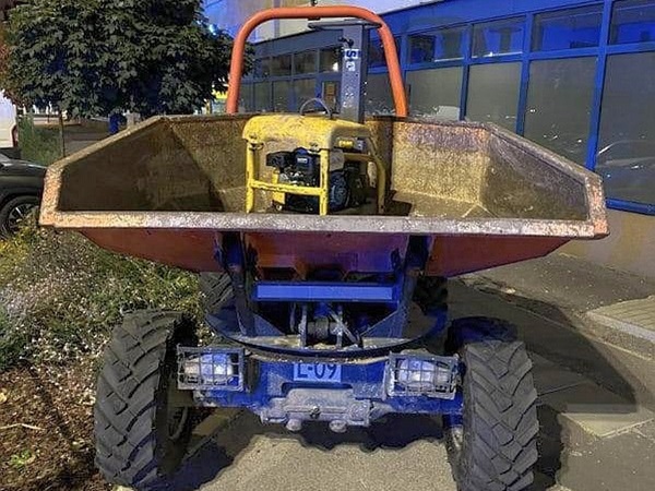 Mała wywrotka z żółtym silnikiem w skrzyni ładunkowej. Ciężarówka jest zaparkowana na utwardzonej nawierzchni.