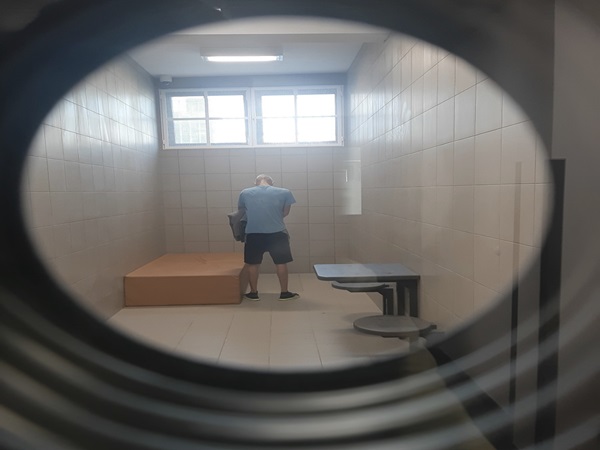 Mężczyzna w celi więziennej, stojący przy małym stoliku i łóżku