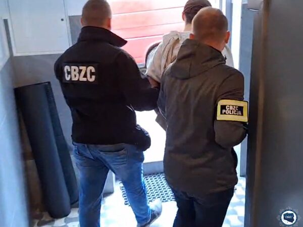 Policjanci eskortujący podejrzanego, widoczne oznaczenia policji CBZC.