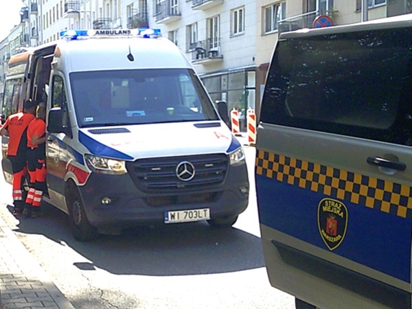 Ratownicy w pobliżu karetki pogotowia i pojazdu policji miejskiej. Numer rejestracyjny: WI 703LT
