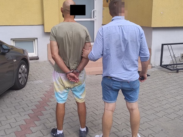 Policjant aresztujący podejrzanego w kajdankach przed budynkiem.