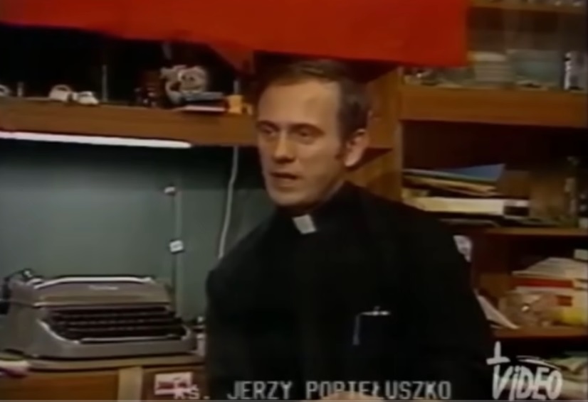 Jerzy Popiełuszko, polski ksiądz, przemawia w słabo oświetlonym pokoju.