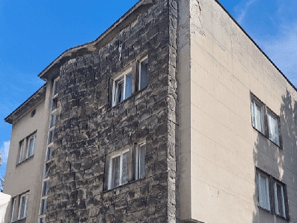 Widok zewnętrzny wielopiętrowego budynku z elewacją z kamienia i betonu.