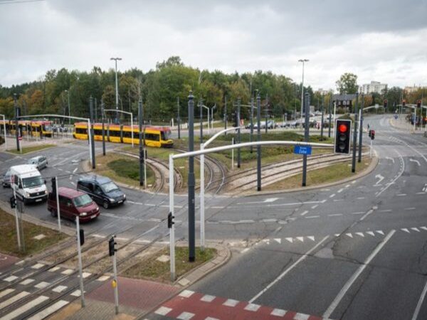 Tramwaj przejeżdżający przez skrzyżowanie w mieście, obok samochodów i sygnalizacji świetlnej.