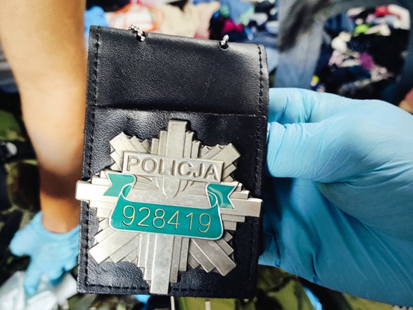 Zbliżenie na polską odznakę policyjną (POLICJA 928419) w czarnym uchwycie.