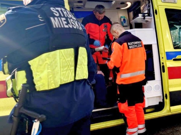 Ratownicy medyczni zajmują się pacjentem w karetce. Na mundurze jednego z ratowników medycznych widoczny jest napis „Ratownik Medyczny”.