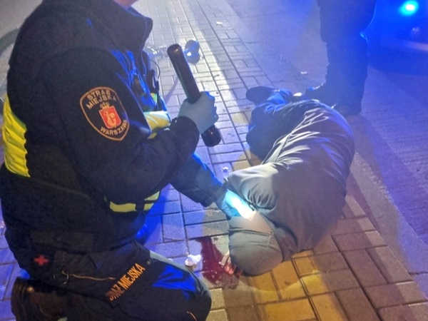 Ratownik medyczny udziela pomocy rannemu na ulicy miasta nocą.