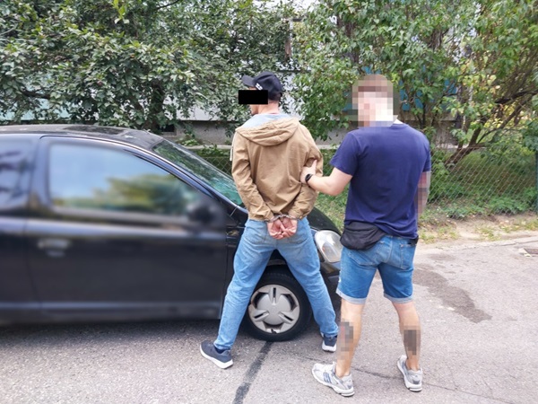 Policjant aresztujący podejrzanego w kajdankach w pobliżu samochodu