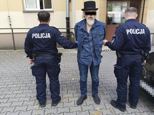 Policjanci aresztujący mężczyznę w kurtce dżinsowej i cylindrze. Na mundurach funkcjonariuszy widoczny jest napis „POLICJA”.