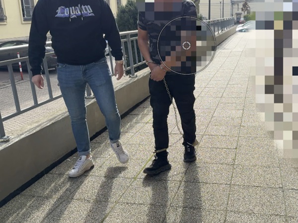 Dwóch mężczyzn w kajdankach, jeden z nich ma na sobie bluzę z kapturem z napisem „Loyalty”, idą chodnikiem.