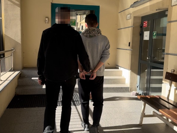 Dwóch podejrzanych skutych kajdankami eskortowanych przez policję.