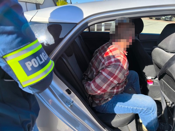 Policjant aresztujący podejrzanego w samochodzie. Na mundurze policjanta widoczny jest napis „POLICJA”.