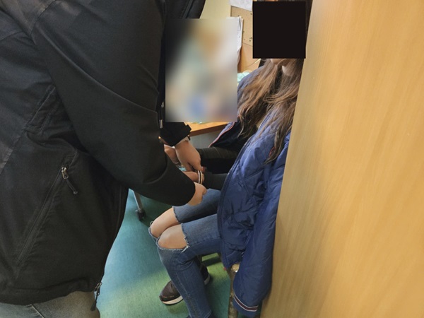 Policjant zakłada kajdanki młodej kobiecie.