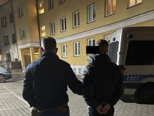 Dwóch podejrzanych w kajdankach, eskortowanych przez policję w nocy.