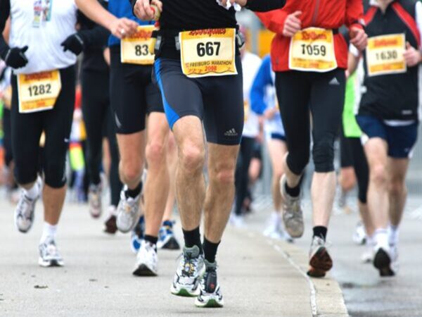 Biegacze rywalizują w maratonie, widoczne są numery startowe.