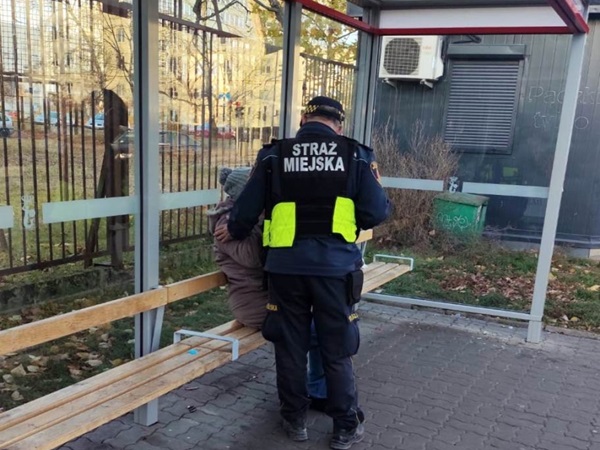 Strażnik miejski pomaga osobie na przystanku autobusowym