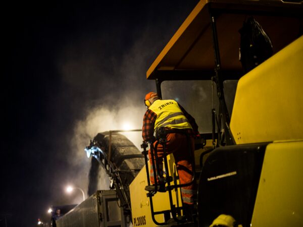 Robotnik drogowy obsługujący maszynę do układania nawierzchni w nocy