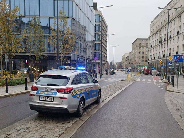 Warszawska ulica miejska z zaparkowanym polskim radiowozem Straż Miejska.