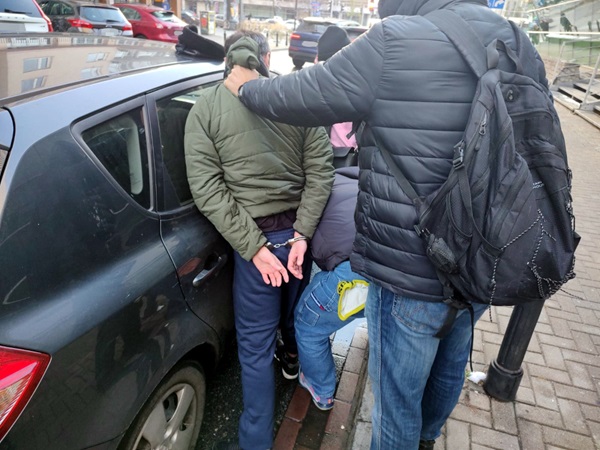 Policjanci zatrzymują podejrzanego w kajdankach w pobliżu samochodu.