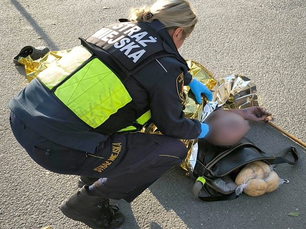 Ratownik pomagający rannej osobie owiniętej w koc termiczny. Na mundurze ratownika widoczny jest napis „Straż Miejska”.