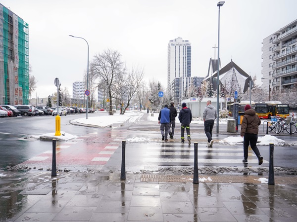 Piesi przechodzący przez zaśnieżoną ulicę miasta zimą.