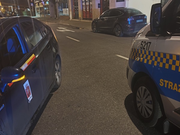 Nocna kontrola drogowa: Policyjny furgon i taksówka zatrzymane obok Tesli.