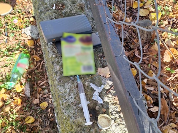 Porzucone przyrządy do zażywania narkotyków, w tym strzykawka, power bank i opakowania, w pobliżu ogrodzenia.