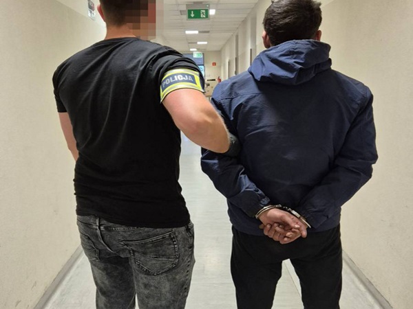 Policjant eskortujący podejrzanego w kajdankach korytarzem