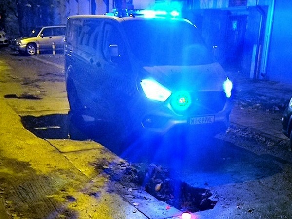 Policyjny furgon nocą oświetla dziurę w drodze.