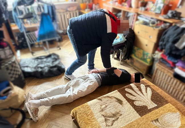 Policjant aresztujący podejrzanego leżącego na podłodze w czasie nalotu.