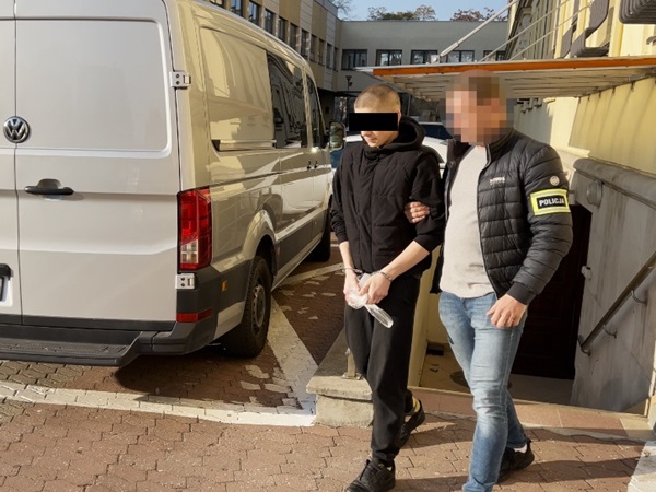 Policja eskortuje podejrzanego w kajdankach w pobliżu furgonetki