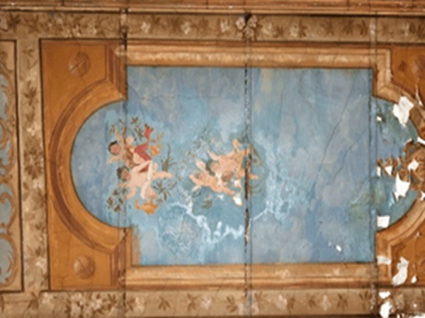 Zniszczony fresk przedstawiający cherubiny bawiące się wśród chmur i detali kwiatowych. Widoczne ślady starzenia i pogorszenia.