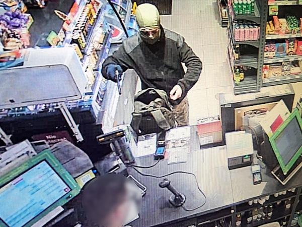 Zamaskowany złodziej włamujący się do sklepu spożywczego trzyma broń przy ladzie.