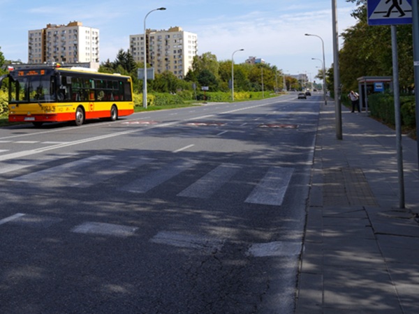 Autobus miejski na ulicy z przejściem dla pieszych, w tle budynki mieszkalne.