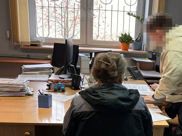 Dwie osoby pracują przy zagraconym biurku, przeglądając dokumenty.