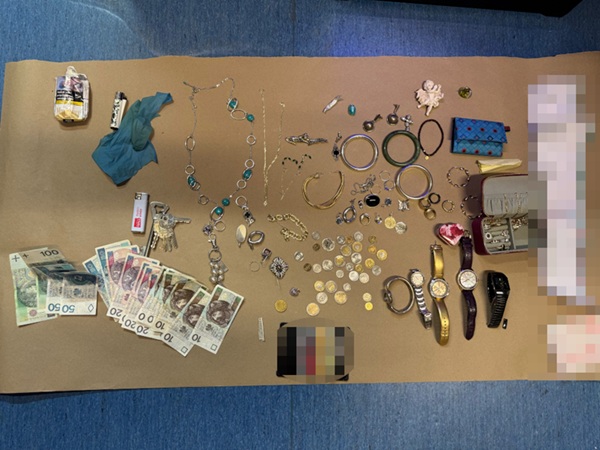 Odzyskano skradzioną biżuterię, zegarki, gotówkę i inne przedmioty ułożone na brązowej powierzchni jako dowód.