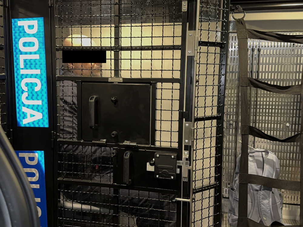 Więzień w policyjnej klatce transportowej. POLICJA