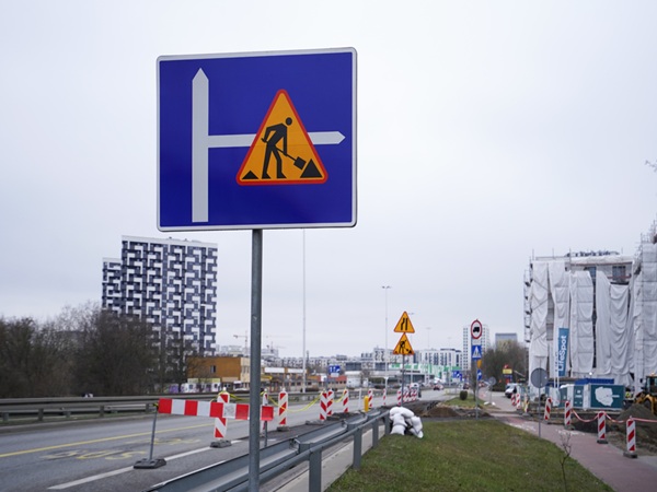Trwają prace drogowe: Robotnicy i oznakowanie informują o zamknięciu pasa.