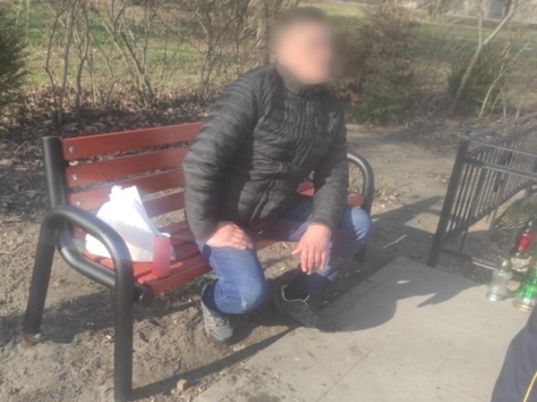 Osoba siedząca na ławce w parku z torbą i napojami