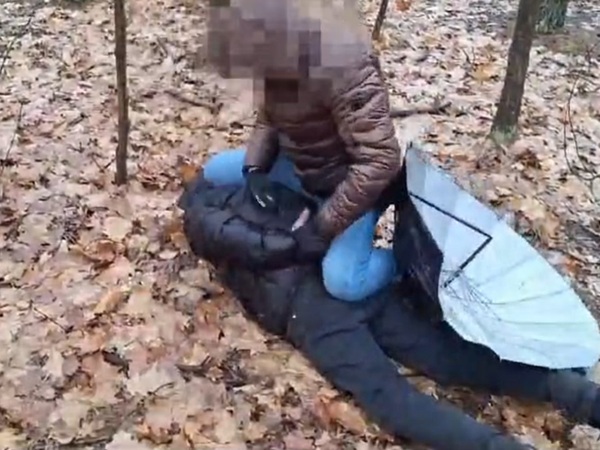 Osoba powstrzymująca inną osobę na ziemi w zalesionym terenie.